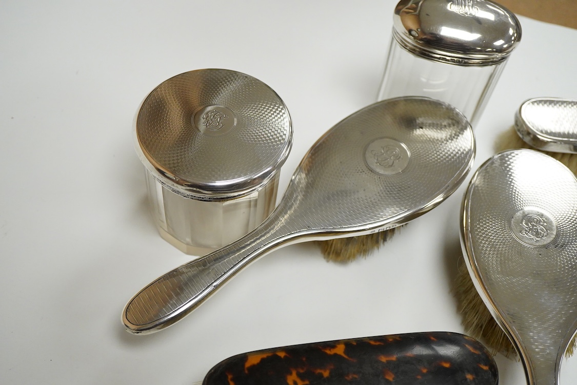 A George V seven piece silver mounted toilet set by Charles Henry Dumenil, comprising a hand mirror, four brushes, a glass toilet jar and button hook, London, 1911/12 & 18, together with one other silver mounted toilet j